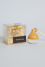 Wooden diffuser with 'Chardonnay' label next to its packaging on a light gray background